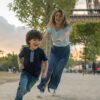 Happy mother and son playing in Paris near the Eiffel Tower chasing each other and smiling