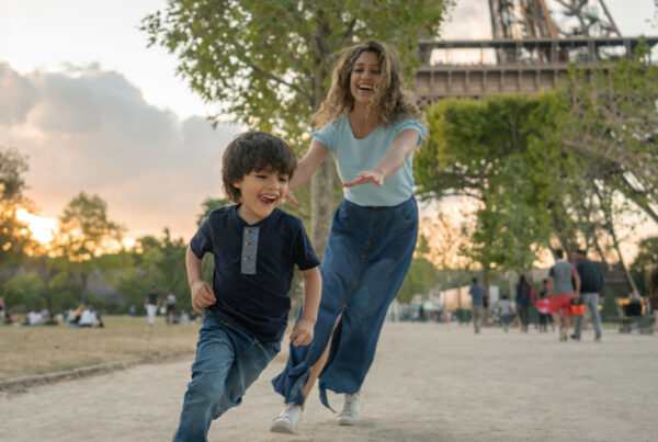 Happy mother and son playing in Paris near the Eiffel Tower chasing each other and smiling