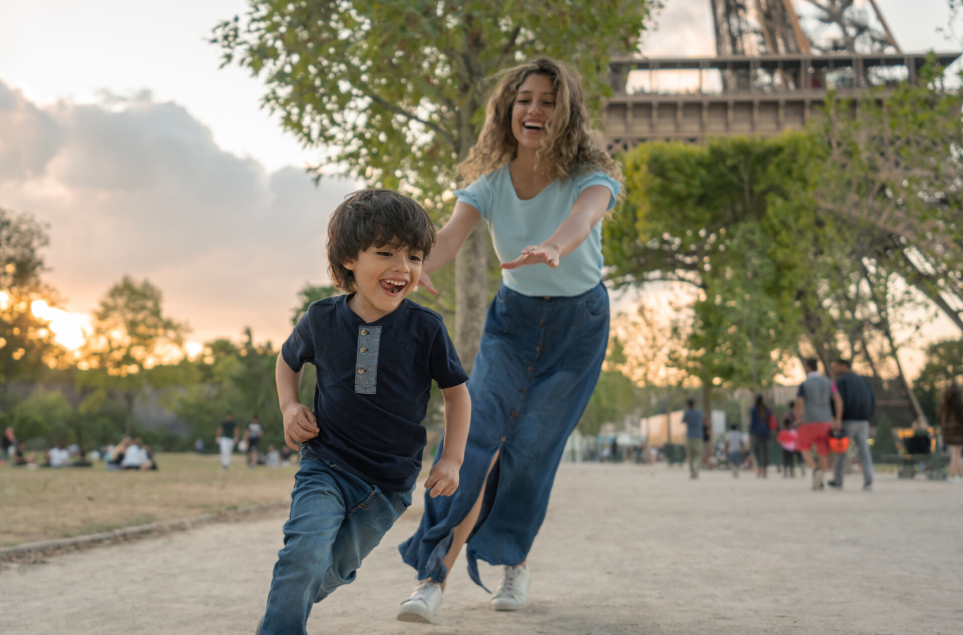 Happy mother and son playing in Paris near the Eiffel Tower chasing each other and smiling