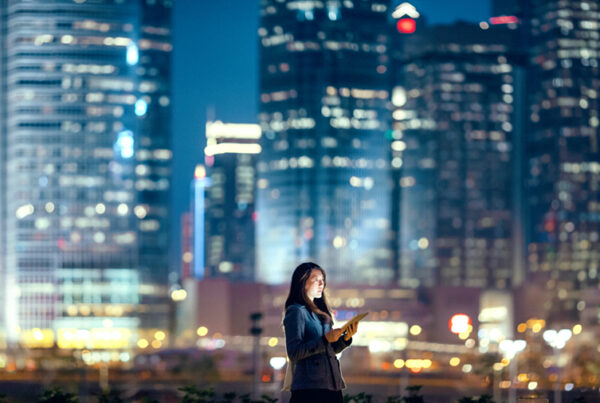 Young businesswoman using digital tablet in financial district, against illuminated corporate skyscrapers at night